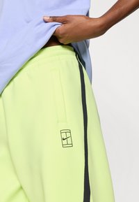 Φωσφορίζοντα κίτρινα παντελόνια τζόγκινγκ με μαύρη πλευρικ ή ρίγα και μικρό μαύρο λογότυπο Nike, με ελαστική μέση και πλαϊνή τσέπη.