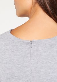 Robe grise en tissu texturé, avec un col rond et une fermeture éclair au dos pour un enfilage facile.