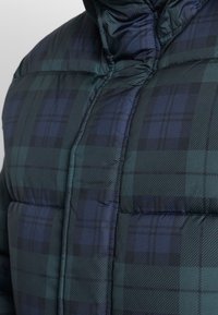 Fodrad pufferjacka med ett mörkgrönt och marinblått rutmönster, som visar kragen och axelområdet.