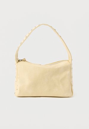 Kleine beige Ledertasche mit einem einzigen Riemen und silbernen Nieten entlang der Kanten und des Riemens, vor einem schlichten Hintergrund.