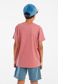 Rode gemêleerde katoenen T-shirt met korte mouwen, gedragen met blauw-grijze elastische shorts. De achterkant toont een relaxte pasvorm en een eenvoudig ontwerp.