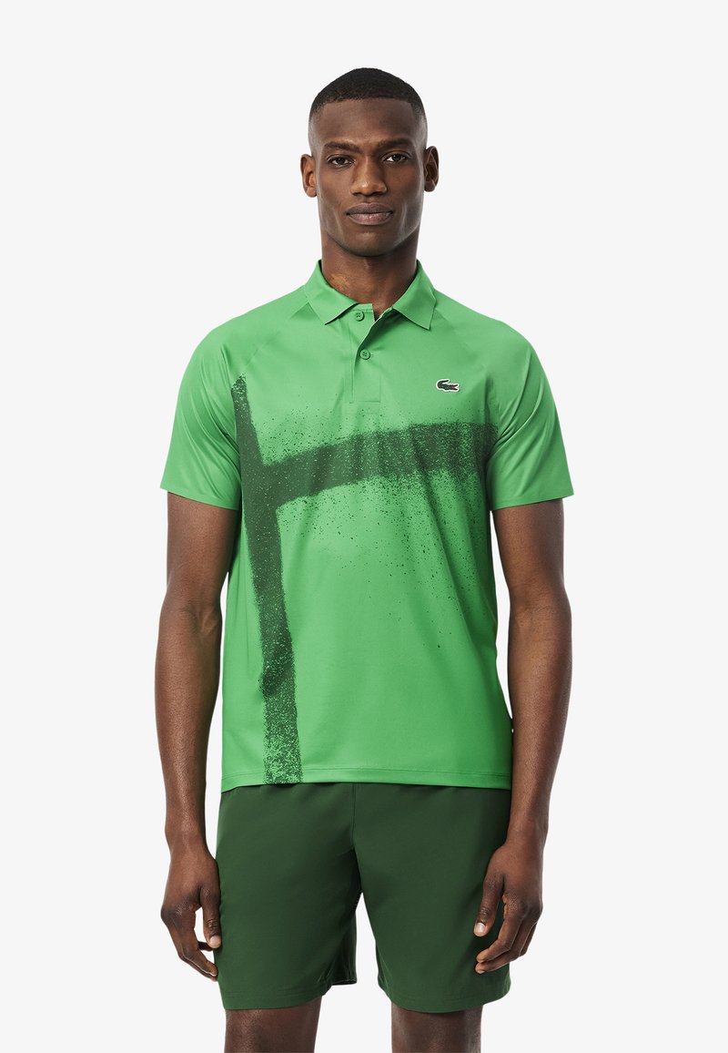 Polo verde de tela suave con un diseño de pinceladas en verde oscuro. Combinado con pantalones cortos verdes oscuros. Logo en el pecho.
