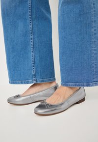 Ballerine argento con finitura liscia, punta rotonda e un nastro decorativo. Abbinato a pantaloni ampi in denim chiaro.
