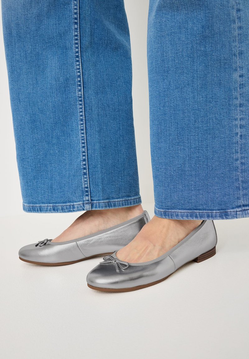 Ballerine argento con finitura liscia, punta rotonda e un nastro decorativo. Abbinato a pantaloni ampi in denim chiaro.