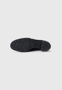 Zapatilla negra con una suela de goma texturizada que presenta un patrón antideslizante. La parte superior tiene un acabado de tela suave y un diseño de perfil bajo.