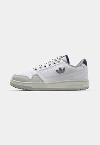 Zapatilla blanca de cuero con detalles en ante gris, puntera redondeada, suela de goma gris y lengua en azul marino. Presenta detalles perforados y un logo.