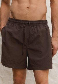 Bruine zwembroek van lichtgewicht stof, voorzien van een elastische tailleband met trekkoord, zijzakken en een relaxed fit.