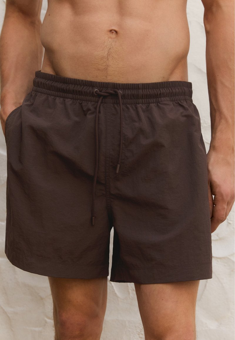 Bruine zwembroek van lichtgewicht stof, voorzien van een elastische tailleband met trekkoord, zijzakken en een relaxed fit.