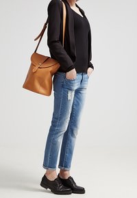 Kožená taška na rameno v hnědé barvě s klopou, nošena s černým topem a černým sakem. Světle modré džíny s poškodeným vzhledem a černé šněrovací boty.