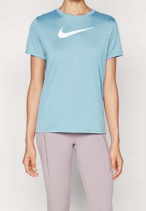 Person iført en lyseblå Nike t-shirt med korte ærmer og lyse lilla leggings står med armene afslappet ned langs siderne.