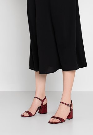 Sandales à talons hauts à imprimé serpent rouge avec une bride à la cheville, un talon carré, un design à bout ouvert et une texture lisse.