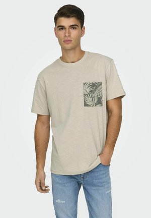 T-shirt beige chiaro con scollo rotondo, caratterizzato da una tasca sul lato sinistro del petto decorata con un motivo di foglie verdi. La vestibilità è comoda.