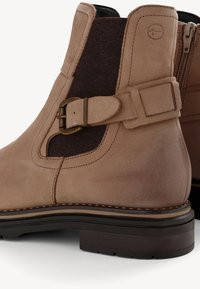 Beige Wildleder Stiefeletten mit einem braunen Stoffpanel, ausgestattet mit einer Metall-Schnalle und Nähakzenten, runder Zehenform und einem niedrigen Blockabsatz.
