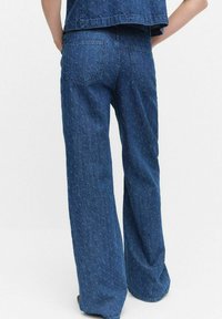 Bredbeniga blå denimjeans med ett strukturerat mönster, bakfickor och en subtil tvättningseffekt, som visar en avslappnad och ledig passform.