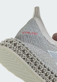 Lys grå strikket overdel med tekstureret finish, prydet med rødt "STRUNG" logo. Grå mesh mønster på sålen med et dristigt, futuristisk design.