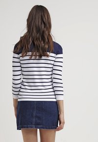 Randig långärmad topp med marinblå och vita horisontella ränder, i kombination med en mörk denimkjol. Slen struktur, figurnära design.