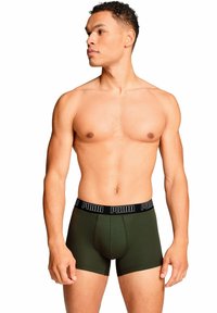 Bóxer de algodón verde con cinturilla de logo negro de Puma. Diseño ajustado, longitud a mitad del muslo, textura suave y sin patrones ni acentos visibles.