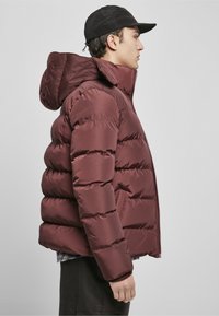 Chaqueta de plumas burdeos con capucha, que presenta un cierre de cremallera en el frente, un patrón de acolchado horizontal y puños acanalados. Textura de tela suave y brillante.