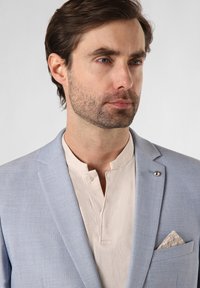Light blue blazer with a structured shape, paired with a cream henley shirt. Notable pocket square displays a pastel geometric pattern.