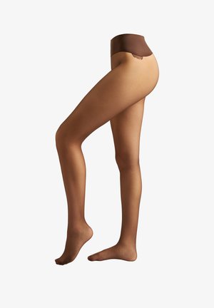 Beine, die durchsichtige braune Feinstrumpfhosen mit einem dunkler braunen Bund tragen, ein Fuß flach auf dem Boden und der andere auf den Zehenspitzen erhoben, vor weißem Hintergrund.