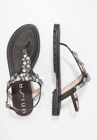 Svarta platta sandaler med en texturerad fotbädd, dekorerade med silverfärgade stenar på remmarna och en gummisula med möntring för bra grepp.