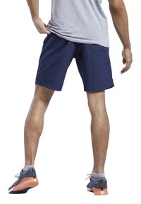 Μπλε σορτσάκια φτιαγμένα από ελαφρύ υλικό, με λεία υφή, κανονική γραμμή και πλαϊνές τσέπες. Φοριούνται με γκρι και πορτοκαλί αθλητικά παπούτσια.