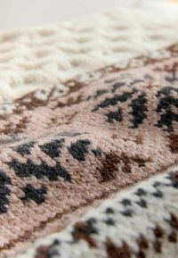 Knit blanket in cream, pink, brown, and grey. Features geometric patterns with textured sections and a soft, fuzzy surface.