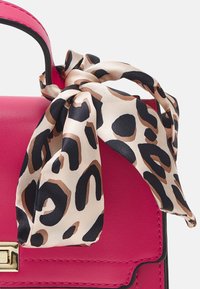 Rosa läderhandväska med svart kant, med en leopardmönstrad silkescarf knuten vid handtaget. Guldaccenter framtill.