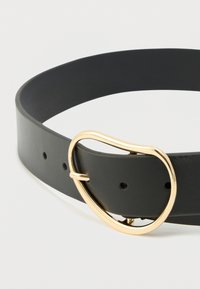 Svart lærbelte med uregelmessig ovalformet gullspenne, delvis festet mot en ensfarget hvit bakgrunn.