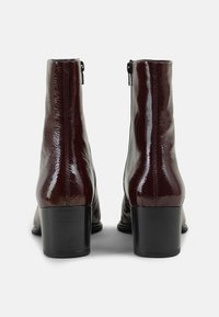 Bordeaux lakleren enkellaarsjes met een vierkante neus, zijknippers en een gestructureerde afwerking. Zwarte blokhakken bieden stabiliteit en hoogte.