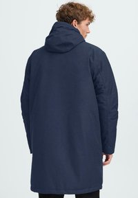 Temno moderna dolga bunda s kapuco, z gladko teksturo, spušenimi rameni in ravno silhueto. Minimalistična zasnova, brez vidne opreme.