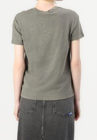 Szara, krótka koszulka z rękawem, z okrągłym dekoltem, wykonana z teksturowanej tkaniny, z lekko wyblakłym wykończeniem i podwiniętymi rękawami.