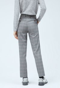Szare spodnie w kratę o dopasowanym kroju, z dwoma tylnymi kieszeniami i gładką fakturą. Noszone z szaro-białymi trampkami.