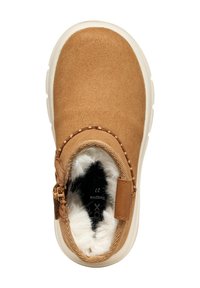 Zapato de ante color beige, tipo slip-on, con forro de felpa, panel elástico en los laterales y punta redondeada. Suela de goma blanca con detalle de costura alrededor del borde.