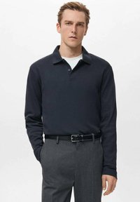 Temno modra polo majica z dolgimi rokavi, ovratnikom in dvema gumboma na zavihku, kombinirana s sivimi hlačami in črnim pasom. Gladek tekstilen material.