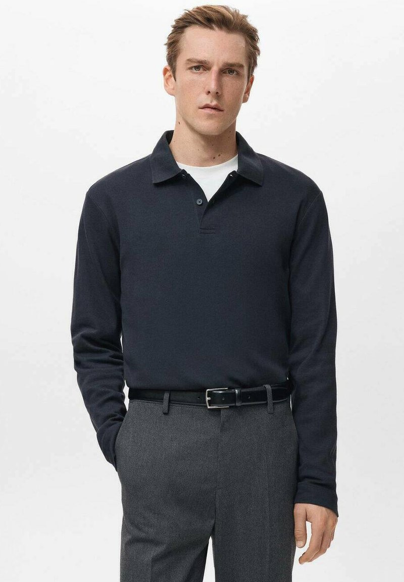 Tricou polo cu mânecă lungă, de culoare bleumarin, cu guler și fente cu doi nasturi, asortat cu pantaloni gri și curea neagră. Textură netedă a țesăturii.