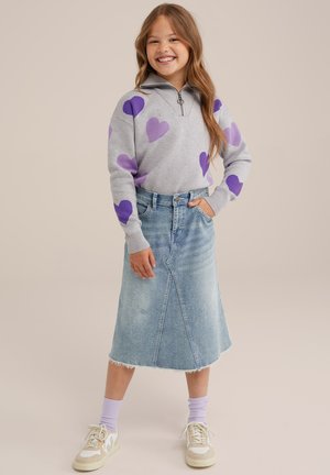 Hanorac gri cu modele de inimă mov, guler cu fermoar; fustă din denim deschis cu tiv destrămat și fante laterale; adidași albi cu accente.