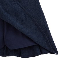 Marinblå texturerad tygöverdrag med ett slätt inre lager. Har en volangkant och en liten dekorativ knapp på sidan.