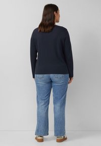 Marineblaues Langarmoberteil mit Rundhalsausschnitt kombiniert mit hellblauen Jeans. Das Outfit wird mit lässigem Schuhwerk mit einer kontrastierenden Sohle abgerundet.