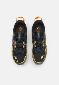 Zapatillas de correr negras con acentos amarillos, parte superior de malla texturizada y cordones turquesa. Cuenta con un bucle frontal y un logo reflectante en el lateral.
