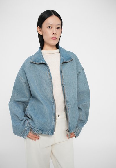 Denim jakna svijetloplave boje, s patentnim zatvaračem sprijeda, visokim ovratnikom, oversized kroja, sa bočnim džepovima. Nosila se preko krem pullovera i bijelih hlača.