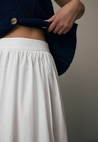 Pullover blu navy a maglia con bottone in evidenza, indossato sopra una gonna bianca plissettata. Focus sulla texture e sui colori, enfatizzando i dettagli del tessuto.