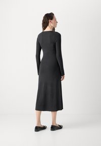 Long-sleeve, dark gray knit dress with a straight cut, ending mid-calf. Smooth texture and minimal seams. Worn with black flats.
