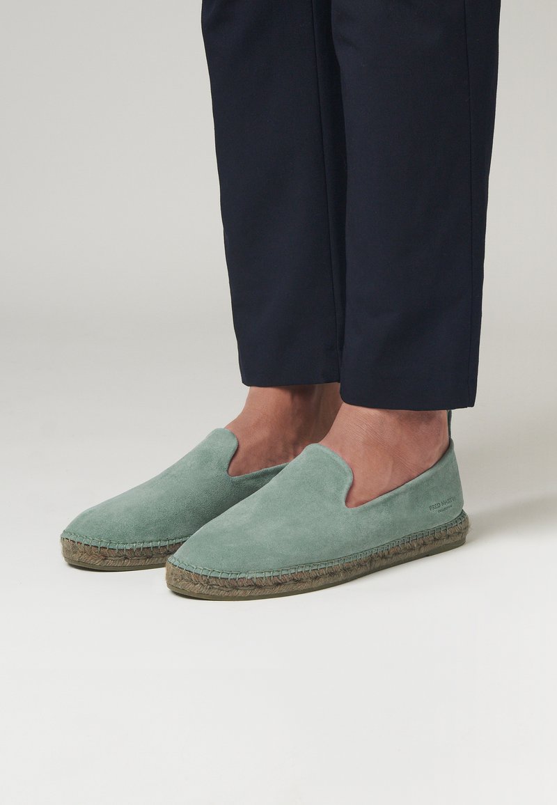 Scarpe slip-on in suede verde con una suola in juta intrecciata in stile espadrille, caratterizzate da una punta rotonda e design con tallone aperto.