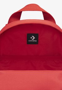 Εσωτερικό κόκκινου σακιδίου πλάτης με μαύρη ετικέτα λογότυπου Converse, υφασμάτι νη υφή και τσέπη με φερμουάρ στο κάτω μέρος για οργάνωση.