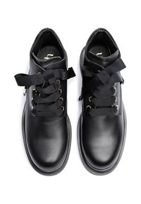 Black leather shoes with wide black ribbon laces tied in bows, gold eyelets, and rounded toes on a white background.