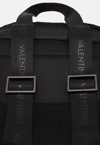 Černý síťovaný batoh s texturovaným povrchem, tkanými popruhy s nápisem "Valentino" a kovovými přezkami pro bezpečné zavření.