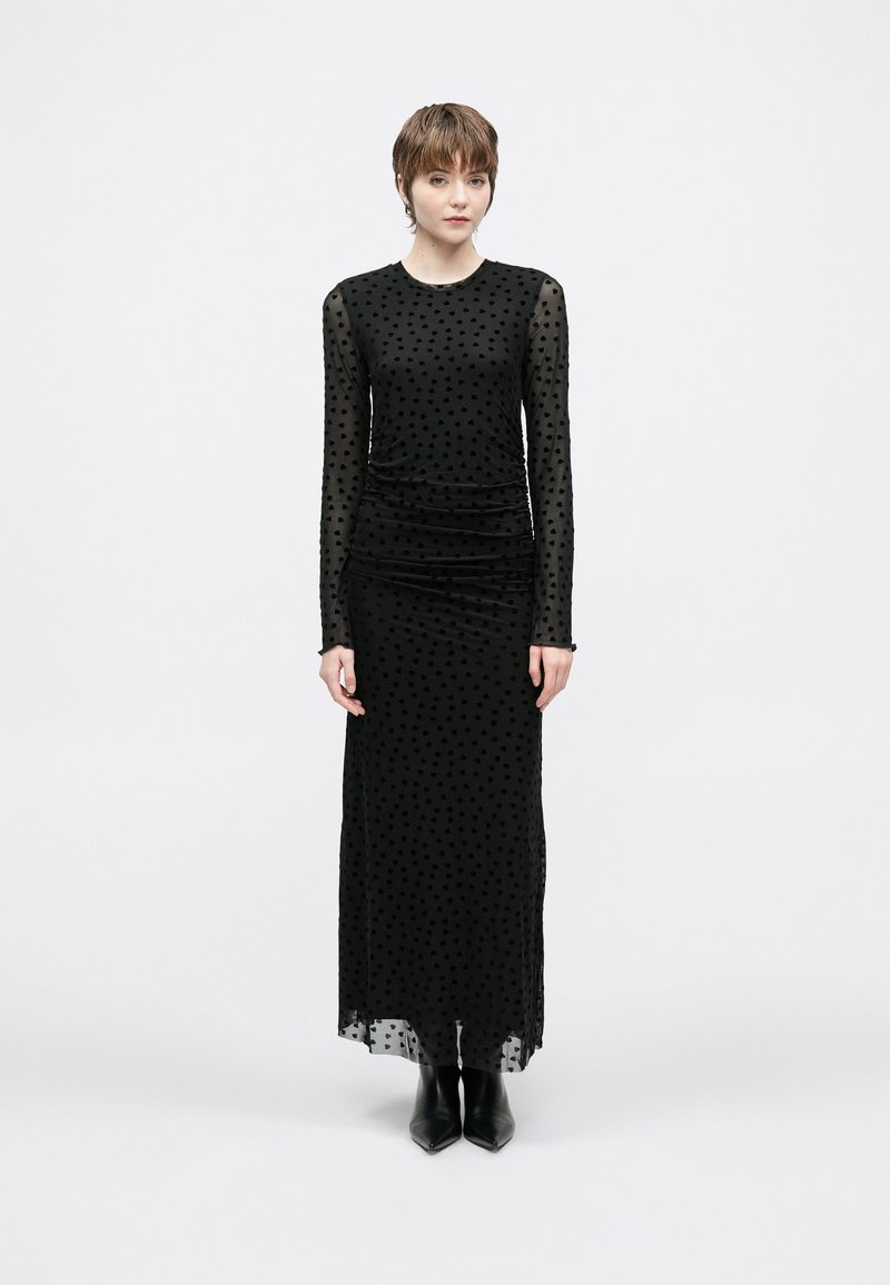Melnas garām piedurknēm kleita ar polka punktu tīkliņa pārklājumu, ručētu vidukli un taisnu siluetu, kopā ar melnām potīšu zābakiem.