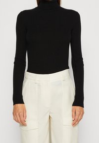 Maglione nero a coste con collo alto e maniche lunghe, dalla vestibilità aderente, in tessuto testurizzato, abbinato a pantaloni cargo crema a gamba larga con tasche frontali.