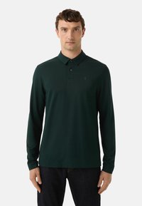 Grünes Poloshirt mit langen Ärmeln aus einem glatten, leichten Stoff; verfügt über einen Knopfkragen und ein kleines Logo auf der linken Brustseite.